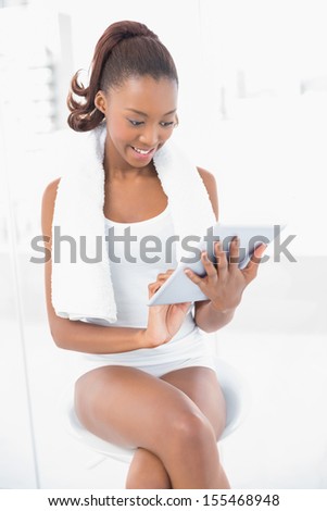 Smiling athletic woman wearing towel using her tablet in bright fitness studio