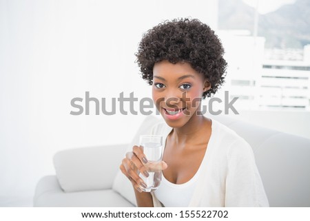 Happy gorgeous brunette holding glass of water sitting on cosy sofa
