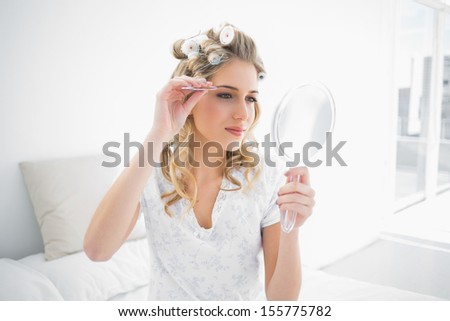 Peaceful natural blonde using tweezers on her eyebrow sitting on cosy bed