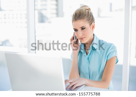 Relaxed smart businesswoman on the phone while using laptop in bright office