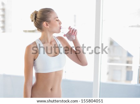 Peaceful young blonde model in white sportswear drinking water
