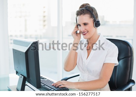 Cheerful call center agent working on computer while having a call in bright office