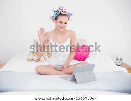 Charming natural brown haired woman in hair curlers chatting online with a tablet pc in bright bedroom