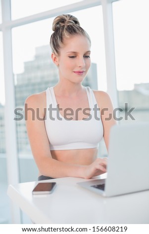 Happy athletic blonde typing on laptop in bright room