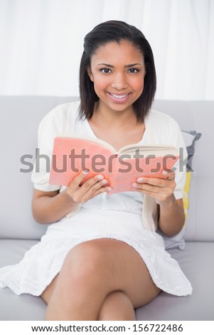 Pretty young dark haired woman in white clothes enjoying a book in a living room