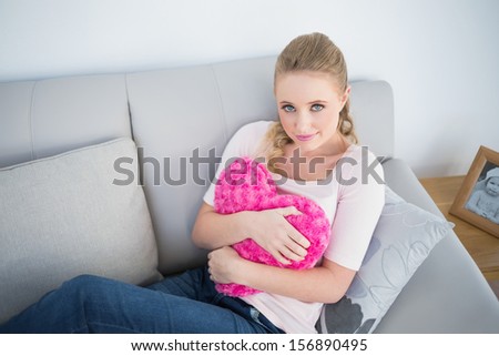 Casual attractive blonde holding heart pillow in bright living room