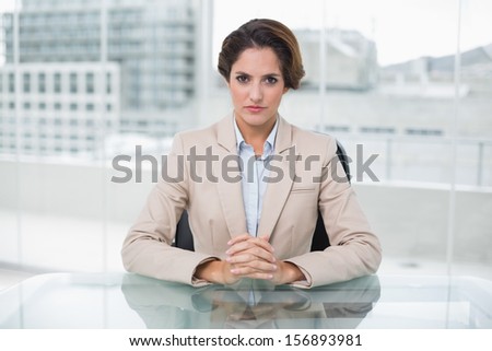 Serious businesswoman looking at camera at her desk in bright office