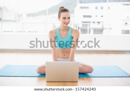 Sporty content woman sitting cross-legged in front of laptop in bright room