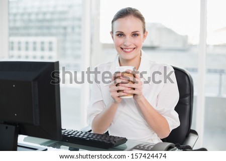 Businesswoman holding disposable cup smiling at camera in her office