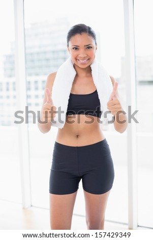 Confident dark haired model in sportswear giving thumbs up in bright fitness studio