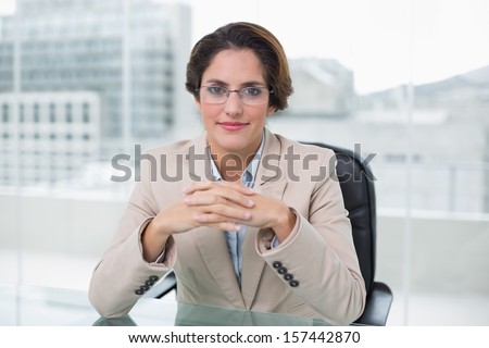 Happy businesswoman sitting at her desk holding her hands together in bright office
