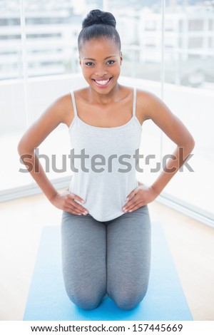 Smiling woman sitting on exercise mat with hands on hip while looking at camera