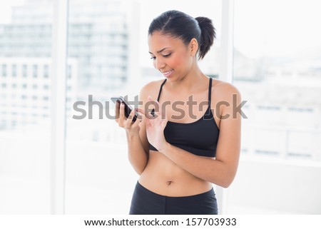 Concentrated dark haired model in sportswear typing on a mobile phone in bright fitness studio