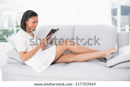 Beautiful young dark haired woman in white clothes reading a magazine in a living room
