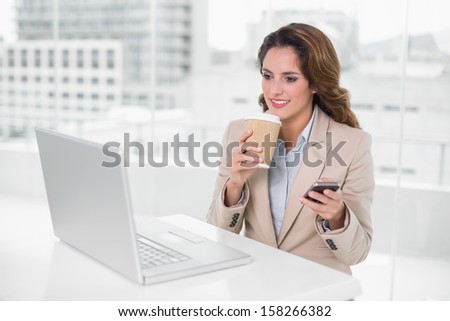 Happy businesswoman holding disposable cup and smartphone in bright office