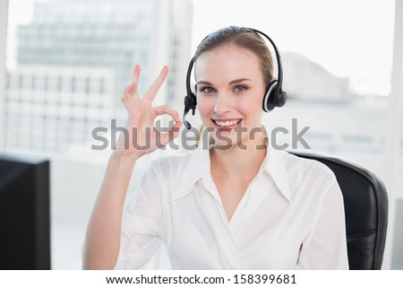 Happy call center agent looking at camera giving ok sign in her office