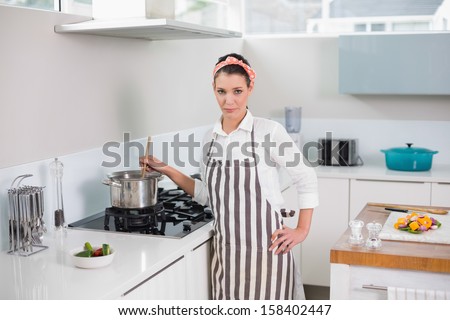 Serious pretty woman with apron cooking in bright kitchen