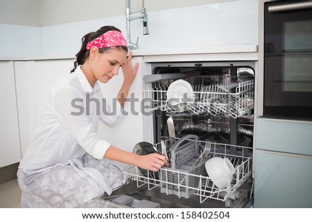 Smiling charming woman using dish washer in bright kitchen
