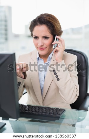 Businesswoman pointing at computer on a phone call in bright office