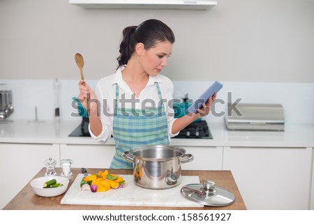 Focused gorgeous woman wearing apron using tablet while cooking in bright kitchen