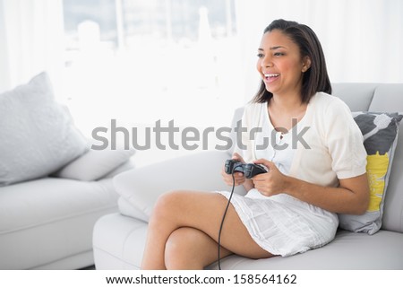 Laughing young dark haired woman in white clothes playing video games in a living room