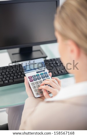 Over shoulder view of businesswoman using calculator in bright office