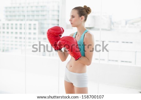Sporty stern woman wearing boxing gloves in bright room