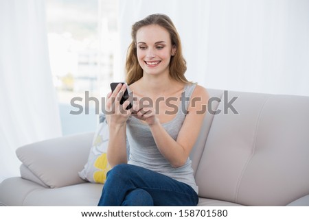 Happy young woman sitting on couch using smartphone at home in the living room