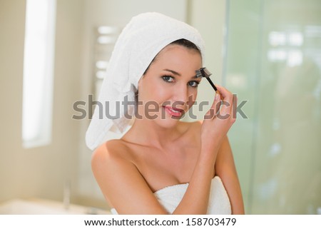 Content natural brown haired woman brushing her eyebrows in a bright bathroom