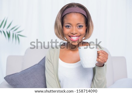 Smiling woman sitting on sofa in bright living room holding mug of coffee