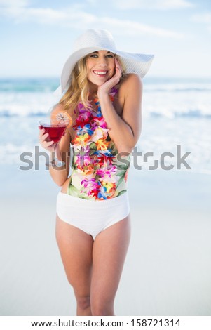 Pleased blonde model in swimsuit holding a cocktail on the beach
