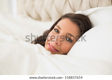 Smiling pretty brown haired woman relaxing in her bed in a bright bedroom