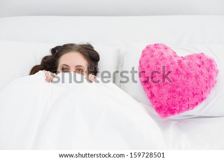 Portrait of a beautiful smiling woman lying in bed with heart  shaped pillow cover