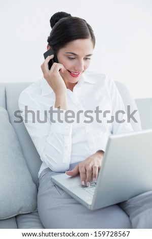 Well dressed young woman using laptop and cellphone on sofa at home