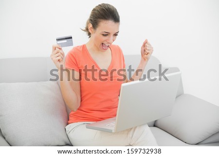 Lovely cheering woman home shopping with her notebook sitting on couch