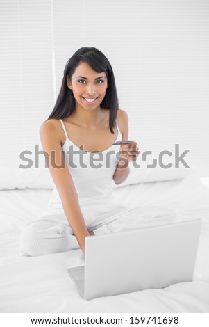 Cheerful lovely woman home shopping with her notebook smiling at camera