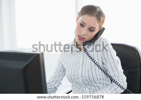 Focused chic businesswoman phoning with telephone while working with computer
