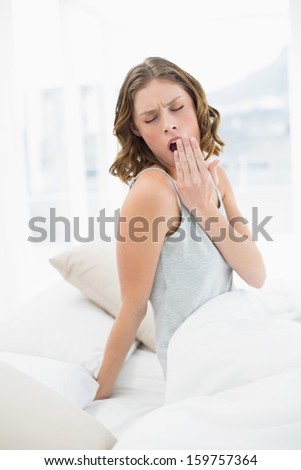 Pretty yawning woman sitting under the cover on her bed in the bedroom