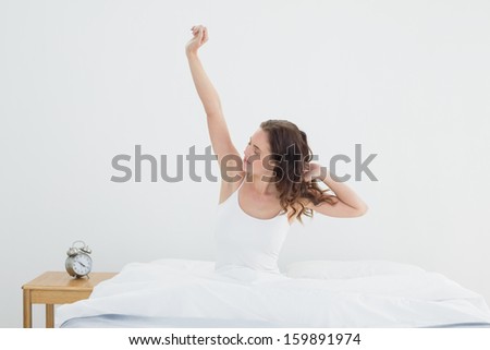 Sleepy young woman waking up in bed and stretching her arms