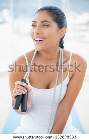 Laughing toned brunette sitting on floor with skipping rope in bright room