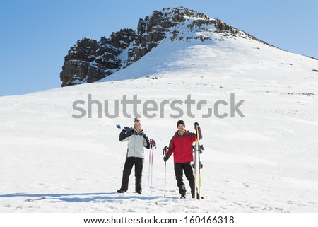 Full length of a couple with ski boards standing on snow covered landscape against clear blue sky