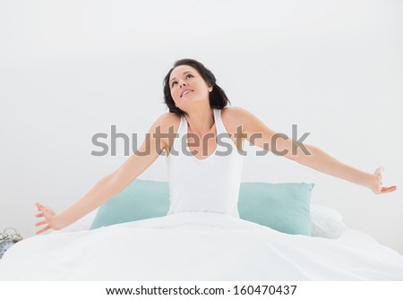 Young woman waking up in bed and stretching her arms