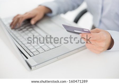 Close-up mid section of a woman doing online shopping through laptop and credit card