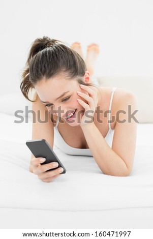 Happy casual young woman looking at mobile phone in bed at home