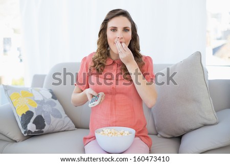 Cute pregnant woman eating popcorn while watching television in the living room