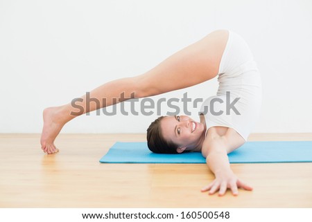 Full length side view of a smiling young woman doing yoga posture on exercise mat