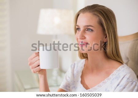 Natural happy woman sitting on bed holding mug in bright bedroom