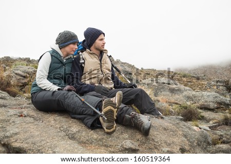 Full length of a young couple sitting on rock with backpack and trekking poles while on a hike