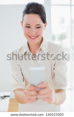 Smiling businesswoman looking at mobile phone in a bright office