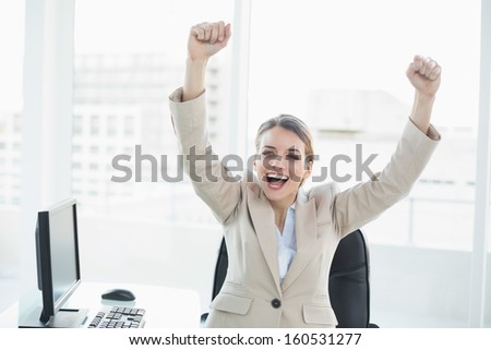Happy cheering woman raising her arms sitting on her swivel chair looking at camera